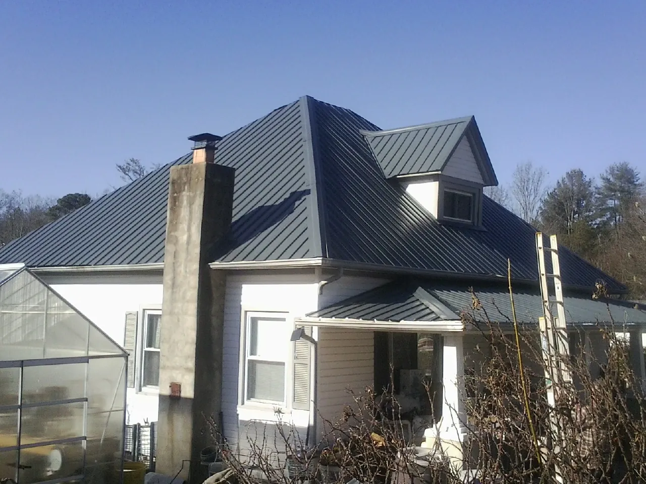 Dark blue standing seam metal roof on a white farmhouse with dormer — Slate & Tile Roof Repair by Roofing Brothers in Omro