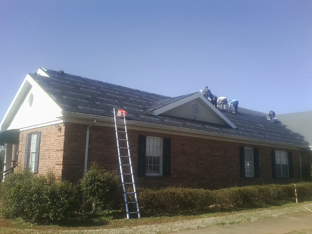 Crew tearing shingles off a brick ranch roof with a ladder set — Emergency Roof Repair work by our crew in Omro