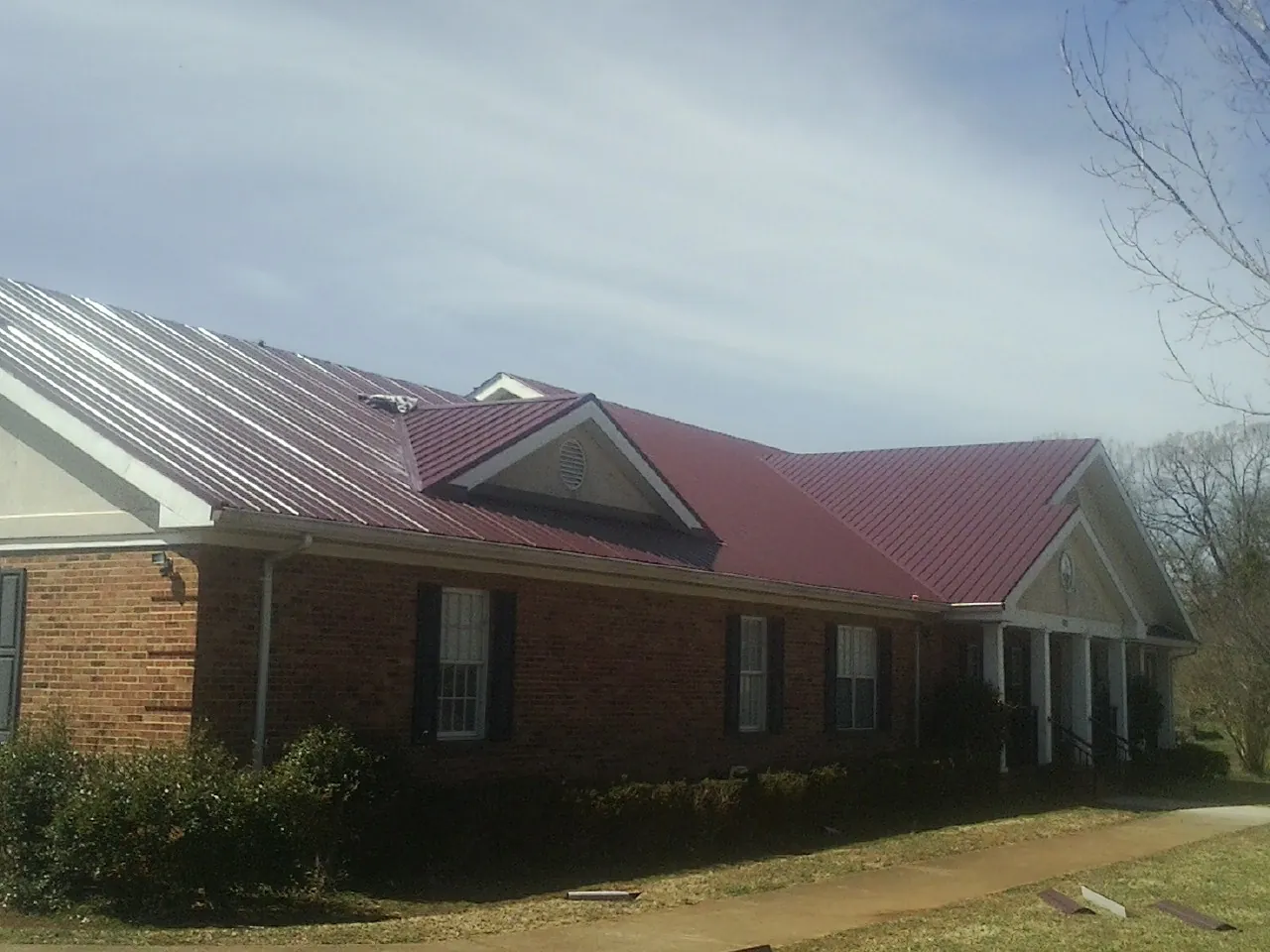 Red metal roof with gabled entries on a long brick building, from a Hail Damage Roof Repair job in Omro