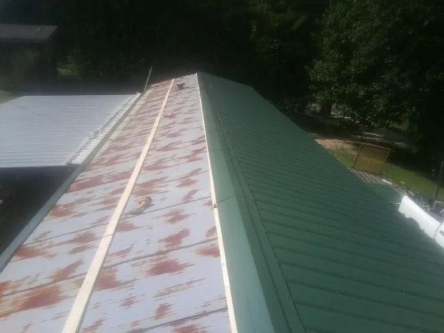 Old rusted panels beside newly installed green metal roofing — Wind Damage Roof Repair by Roofing Brothers in Omro
