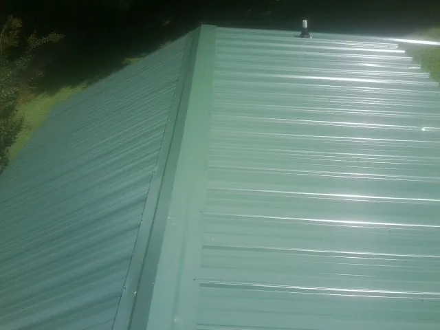 New green metal panels meeting at the ridge of a roof — Flat Roof Repair work by our crew in Omro