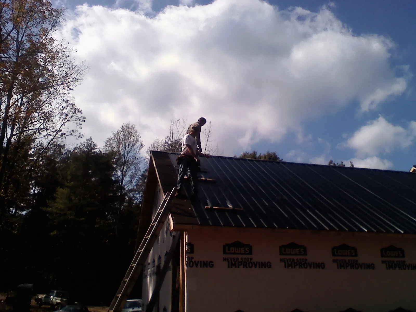 Roofer fastening dark metal panels high against a cloudy sky, from a Roof Inspection job in Omro