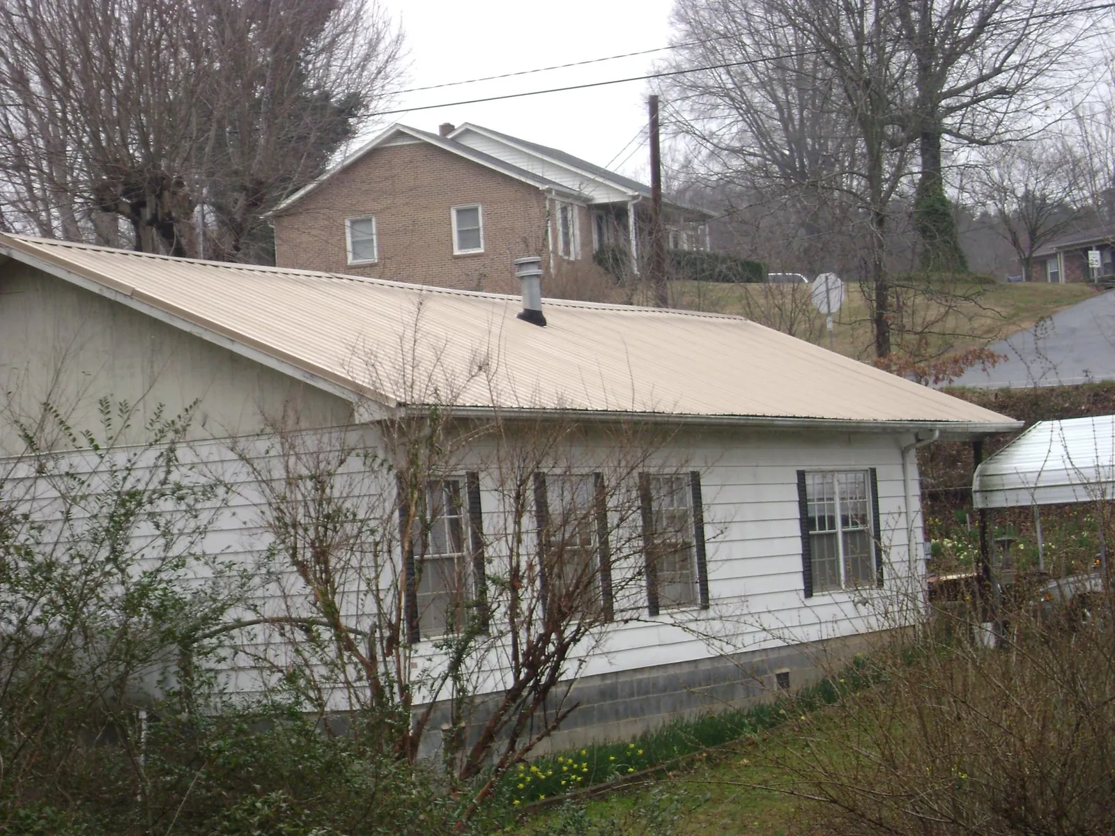 Tan metal roof on a white sided house set into a hillside — Commercial Roofing by Roofing Brothers in Omro