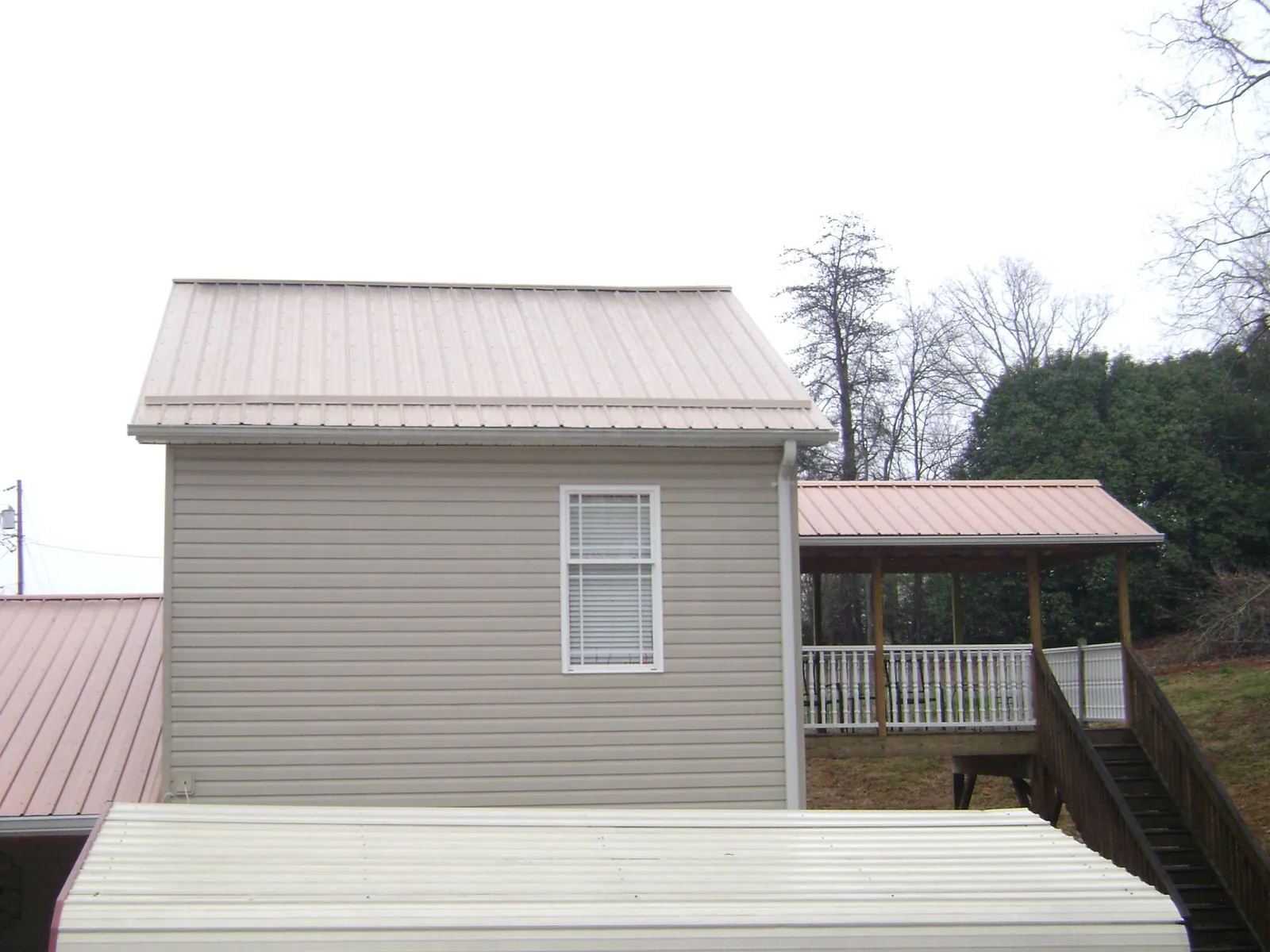 Tan metal roofs on a two story addition and attached porch, from a Roof Replacement job in Omro